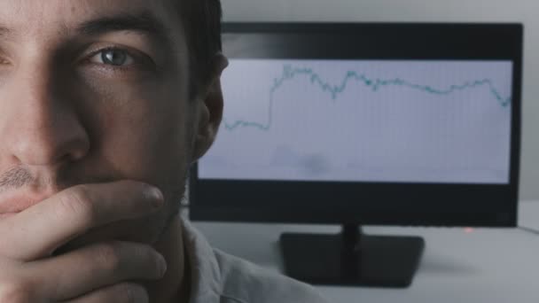 Close-up gezicht van een jonge zakenman tegen de achtergrond van de handel planning op de monitor. — Stockvideo