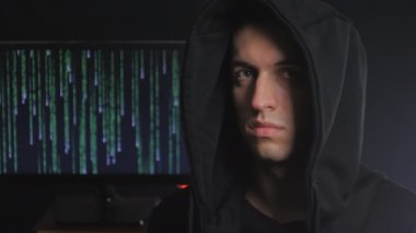 bir anonim hacker'ı olan bir başlık ikili kod arka plan, karanlık bir odada kapalı bir suratla portresi