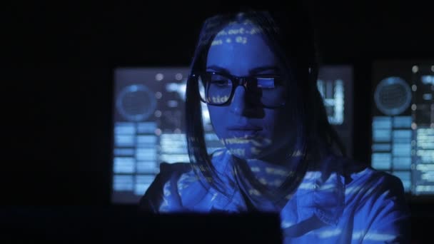 Vrouw Hacker programmeur werkt op computer met cyber security center gevuld met beeldschermen. Binaire code op haar gezicht — Stockvideo