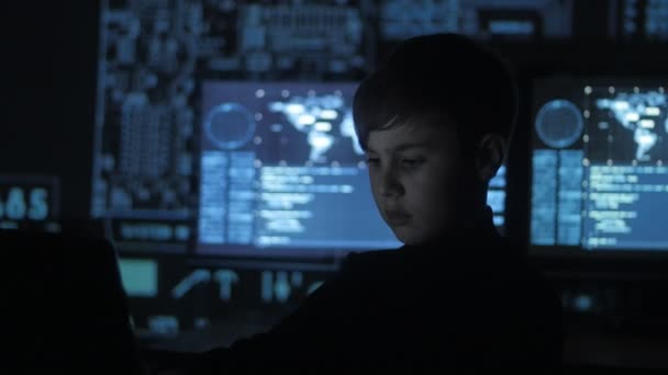 Молодой вундеркинд хакер-программист, работающий за компьютером в дата-центре, заполненном дисплейными экранами. Портрет вундеркинда . — стоковое видео