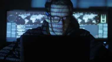 Hacker programcı bardaklarda yüzünü göstermek perde ile dolu siber güvenlik Merkezi'ndeki mavi kod karakterlerini yansıtan bilgisayarda çalışıyor.