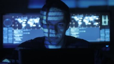 Siber Güvenlik Merkezi'ndeki yüzünde mavi kod karakterlerini yansıtan süre bilgisayar başında çalışan erkek hacker programcı göstermek perde ile dolu.