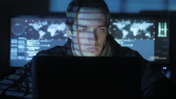 Мужчина-программист, работающий за компьютером, в то время как персонажи синего кода отражают его лицо в центре кибербезопасности, заполненном экранами . — стоковое видео