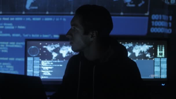 Joven programador Geek Hacker está trabajando en la computadora en el centro de seguridad cibernética lleno de pantallas de visualización . — Vídeos de Stock