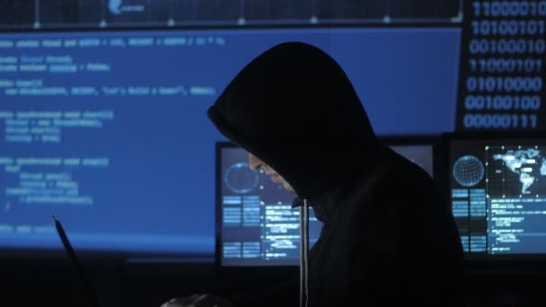 Uomo geek hacker in cappuccio che lavora al computer nel centro di sicurezza informatica pieno di schermi di visualizzazione . — Video Stock