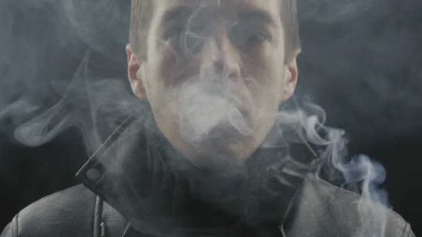 Крупный план молодого человека курит сигареты на черном фоне — стоковое видео