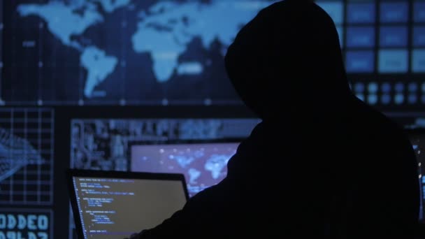 Hombre anónimo geek hacker en la capucha de trabajo en la computadora en el centro de seguridad cibernética lleno de pantallas . — Vídeos de Stock