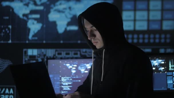 Mens geek hacker in kap werkt op computer in cyber Beveiligingscentrum gevuld met schermen. — Stockvideo