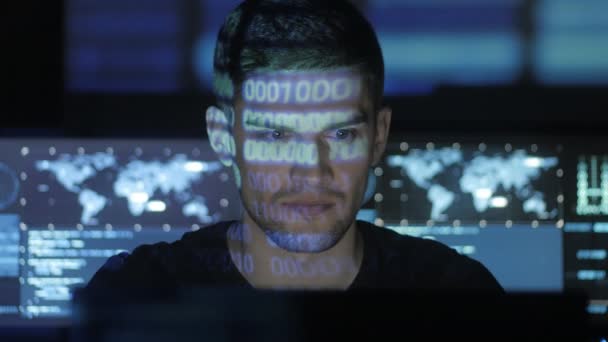 Programador de hackers masculino trabalhando no computador, enquanto personagens de código azul refletem em seu rosto no centro de segurança cibernética preenchido com telas de exibição . — Vídeo de Stock