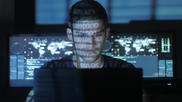 Mannelijke hacker programmeur werkt op computer, terwijl blauw code tekens over zijn gezicht in cyber Beveiligingscentrum nadenken gevuld met schermen. — Stockvideo