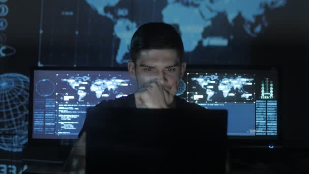 Hacker programmeur in glazen werkt op computer terwijl blauw binaire code tekens over zijn gezicht in cyber Beveiligingscentrum gevuld met schermen nadenken. — Stockvideo