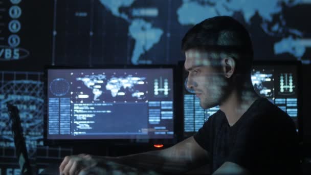 Programador hacker masculino que trabaja en la computadora, mientras que los caracteres de código azul reflejan en su cara en el centro de seguridad cibernética lleno de pantallas de visualización . — Vídeos de Stock