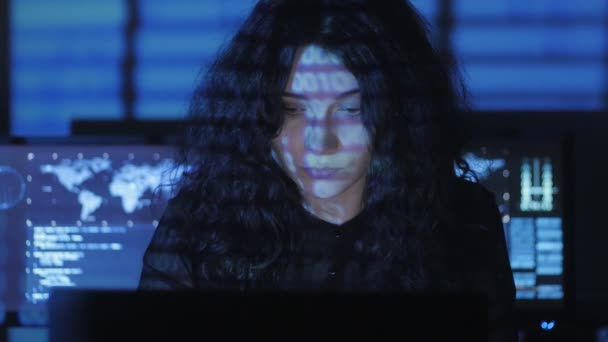 Hacker programátor s kudrnatými vlasy žena pracuje v centru zabezpečení cyber plné obrazovky v počítači. Binární kód na její tváři — Stock video