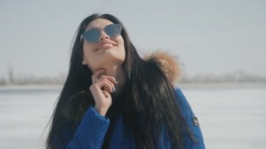 Genç gülümseyen güzel esmer kış, güneş gözlüklü kadın portresi arka plan kar yağıyor..