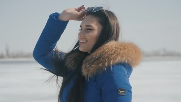 Portret van jonge mooie lachende brunette vrouw in zonnebril op winter sneeuwt achtergrond. — Stockvideo