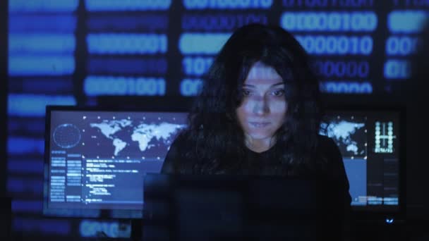 Kvinna Hacker programmerare med lockigt hår fungerar på dator i cyber security center fylld med skärmar. Binär kod på hennes ansikte — Stockvideo
