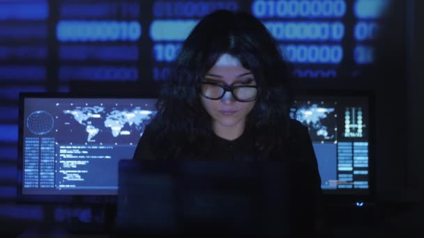 Gebrild vrouw Hacker programmeur werkt op computer met cyber security center gevuld met beeldschermen. Binaire code op haar gezicht — Stockvideo