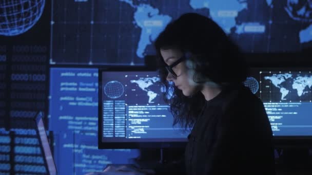 Portret programista młodą kobietę w okularach, pracując przy komputerze w centrum przetwarzania danych wypełnione ekranów — Wideo stockowe