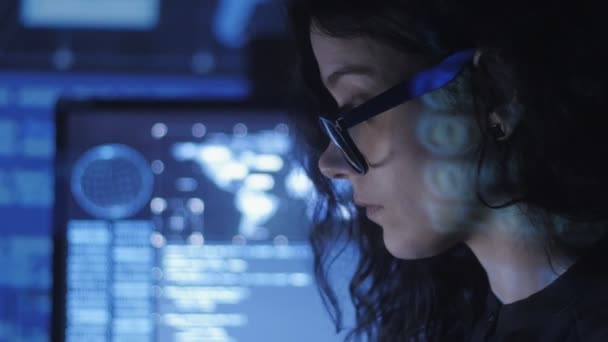 Портрет молодой женщины-программиста в очках, работающей за компьютером в дата-центре, заполненном экранами — стоковое видео