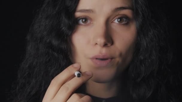 Portrait de jeune femme brune aux cheveux bouclés fume une cigarette et regarde la caméra sur le fond sombre — Video