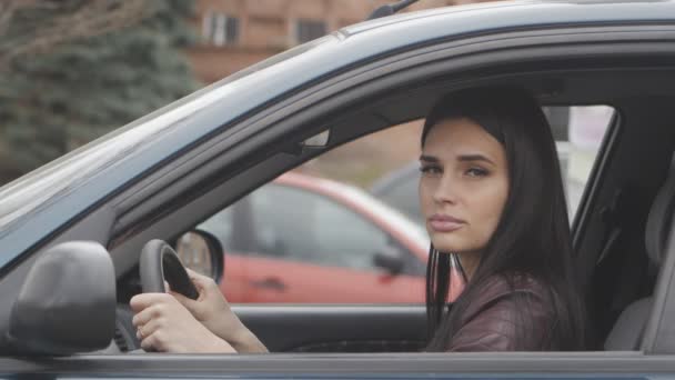 Bella donna bruna si siede in una macchina su un sedile del conducente in città — Video Stock