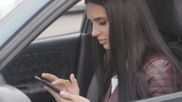 Jovem bela mulher usa um smartphone enquanto sentado em um carro na cidade — Vídeo de Stock