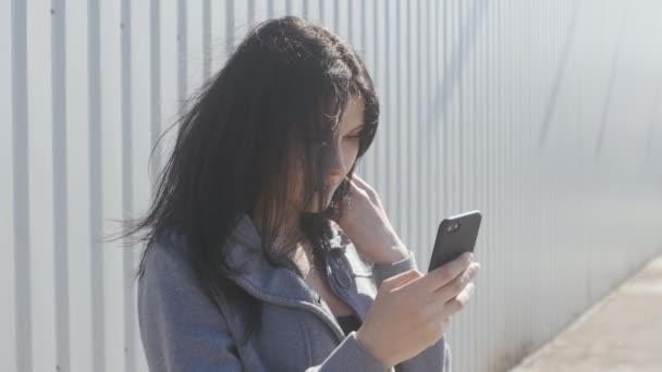 Retrato de mulher morena bonito usando smartphone ao ar livre na rua. O vento facilmente acena seu cabelo . — Vídeo de Stock