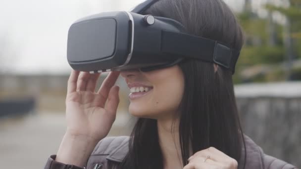 Молодая женщина получает опыт использования VR-гарнитуры или гарнитуры виртуальной реальности на открытом воздухе — стоковое видео