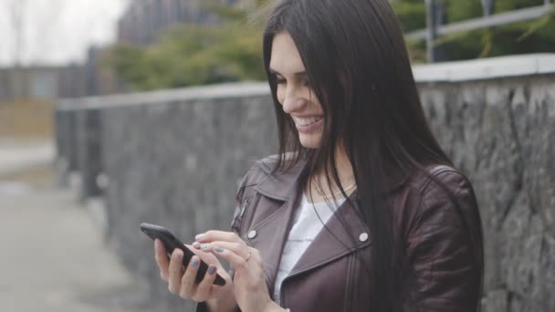 Retrato de una hermosa mujer joven usando el teléfono inteligente al aire libre en la calle. Chica es feliz y sonriente — Vídeos de Stock