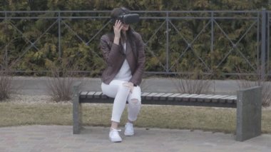 genç kadın Vr-kulaklık ya da kulaklık sanal gerçeklik parkta bankta otururken açık kullanarak deneyim elde