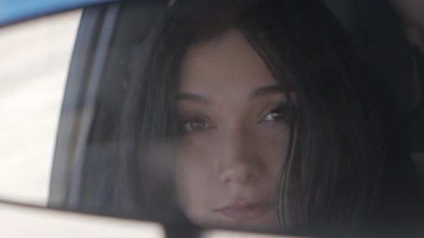 Молодая красивая женщина, сидя в машине, смотрит в зеркало заднего вида — стоковое видео