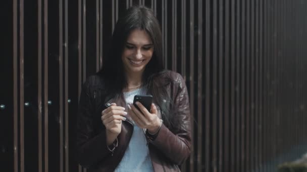 Joven mujer feliz mensajes de texto en el teléfono inteligente en la ciudad — Vídeos de Stock