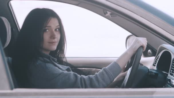 Retrato de una linda joven sentada en un coche detrás del volante en el asiento del conductor . — Vídeo de stock