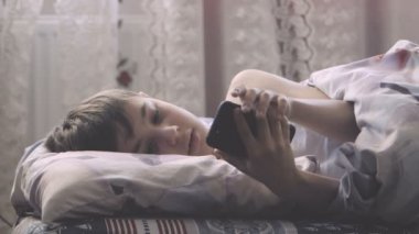 Çocuk sabah yatak odasında yatakta yatıyor ve bir akıllı telefon kullanır.