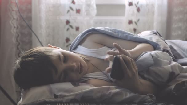 Garçon se trouve dans son lit dans sa chambre le matin et utilise un smartphone . — Video