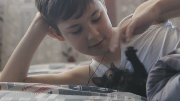 Kleine jongen spelen met een kat in zijn bed in de ochtend slaapkamer — Stockvideo