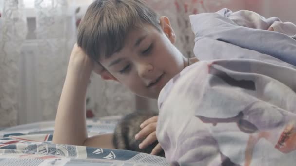 El chico está jugando con el gatito en su cama en el dormitorio. Feliz infancia. — Vídeos de Stock