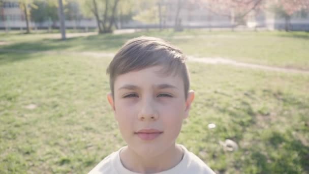 Nahaufnahme Porträt eines Jungen im Alter von 10 Jahren vor grünem Hintergrund im Frühling oder Sommer. — Stockvideo