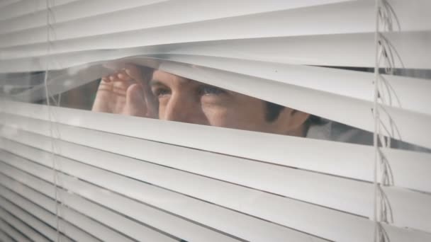 Joven mirando por la ventana a través de las persianas a la calle — Vídeo de stock