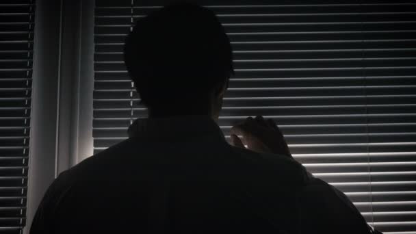 Silhouette of paranoid man looking through blinds — Stock Video