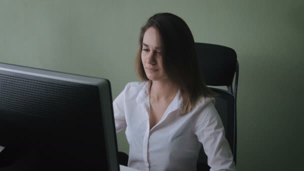 Portrait of young woman in white shirt working at computer in office — Stock Video