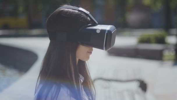 Acercamiento mujer joven con gafas VR, auriculares, jugar juegos virtuales y ver videos al aire libre en la hermosa calle de la ciudad — Vídeos de Stock