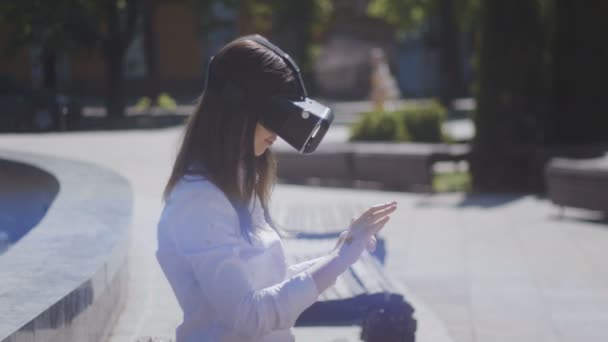 Закрытая молодая женщина в VR очках, гарнитуре, играя в виртуальные игры и просматривая видео на улице на красивой городской улице — стоковое видео
