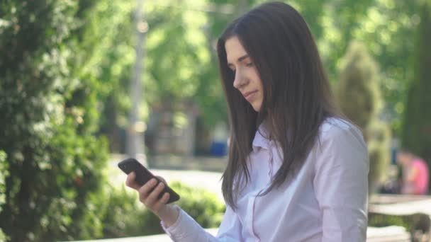 Портрет молодой женщины в белой рубашке использует смартфон во второй половине дня на улице в городе . — стоковое видео