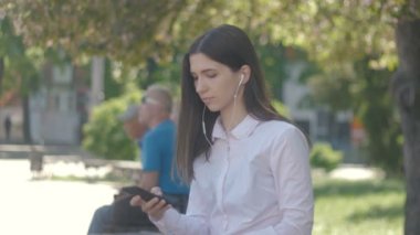 Beyaz gömlekli kulaklık ve akıllı telefon kullanarak müzik genç kadın portresi yan görünüm. City açık