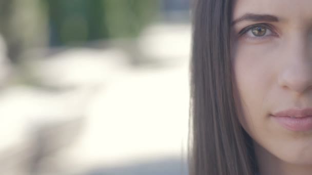 Retrato de cara cortada de una hermosa mujer joven mirando a la cámara al aire libre en la calle de la ciudad. De cerca. Media cara — Vídeo de stock