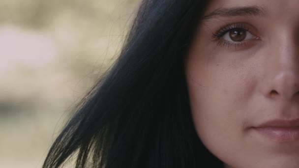 Media cara retrato de mujer joven morena mirando a la cámara y sonriendo sobre fondo borroso al aire libre — Vídeos de Stock