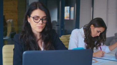 Modern Ofis 'te dizüstü bilgisayarda çalışan çekici genç bir iş kadını. Hazır kahve içiyorum..