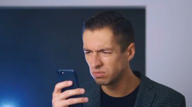 Şok edilmiş ve iğrenmiş bir adamın portresi. Kafası karışmış bir adam akıllı telefonda tatsız bir mesaj görmüş. Görmekten korkuyor. Close.
