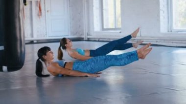 Spor salonunda karın egzersizi yapan iki atletik kadın. Spor kadınları egzersiz minderindeki V-up 'ları yaparak kaslarını geliştiriyor..